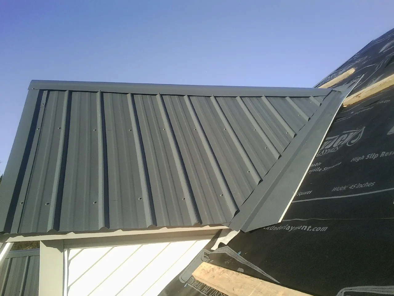 Gray metal roof panels going on over a garage gable in Grass Lake
