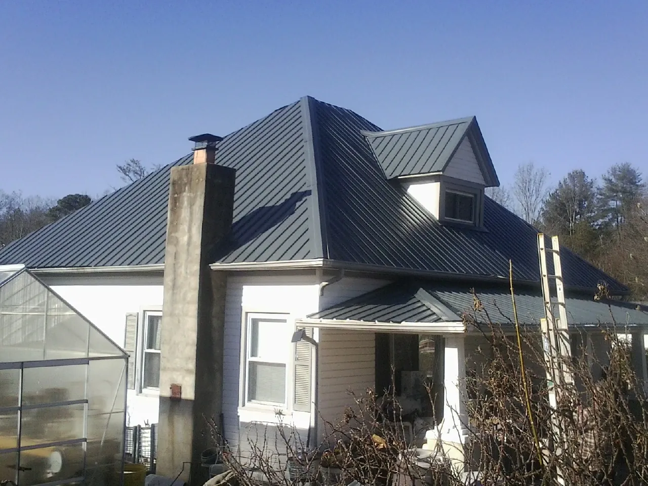 Dark blue standing seam metal roof on a white farmhouse with dormer — Slate & Tile Roof Repair by Roofing Brothers in Grass Lake