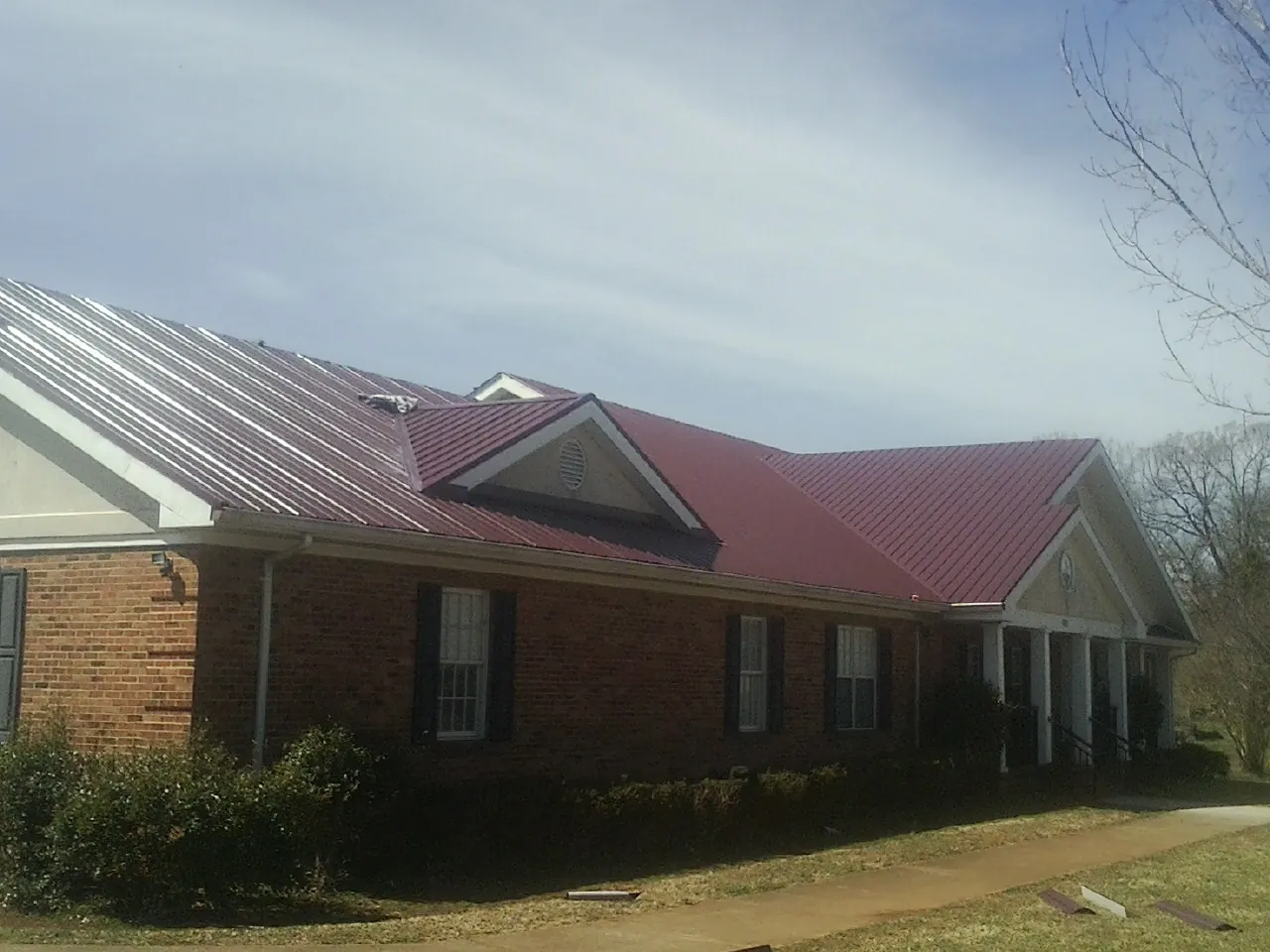 Red metal roof with gabled entries on a long brick building, from a Hail Damage Roof Repair job in Grass Lake