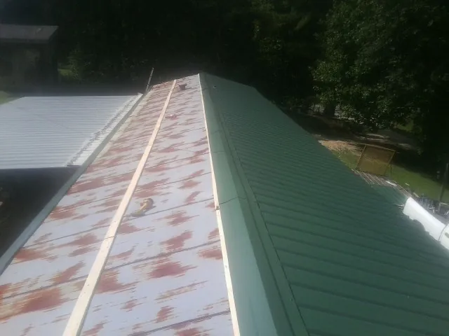 Old rusted panels beside newly installed green metal roofing — Wind Damage Roof Repair by Roofing Brothers in Grass Lake
