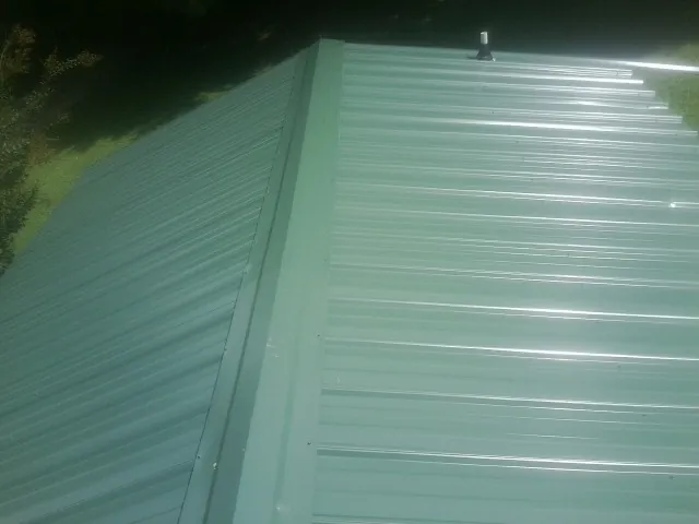 New green metal panels meeting at the ridge of a roof — Flat Roof Repair work by our crew in Grass Lake