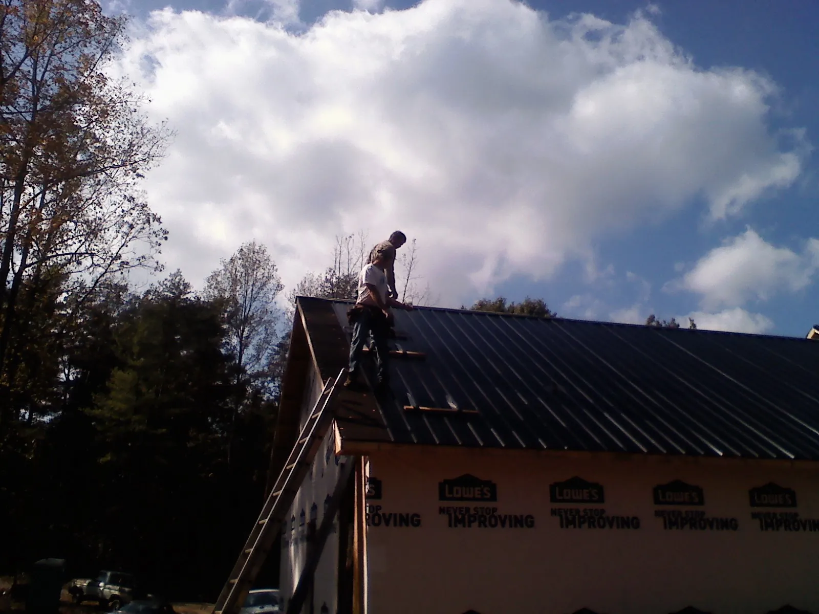 Roofer fastening dark metal panels high against a cloudy sky, from a Roof Inspection job in Grass Lake