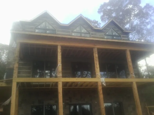Dormers and porch framing on a large log home under construction — Roof Coating work by our crew in Grass Lake
