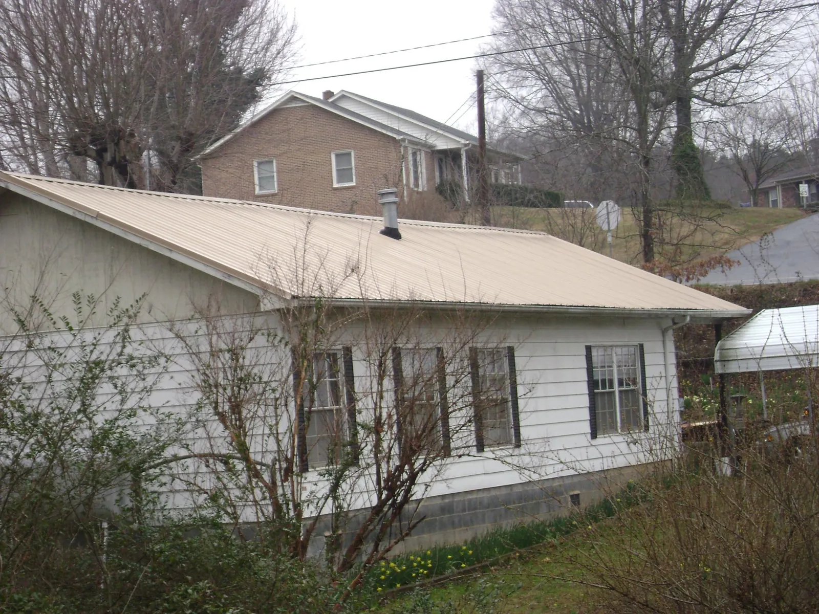 Tan metal roof on a white sided house set into a hillside — Commercial Roofing by Roofing Brothers in Grass Lake