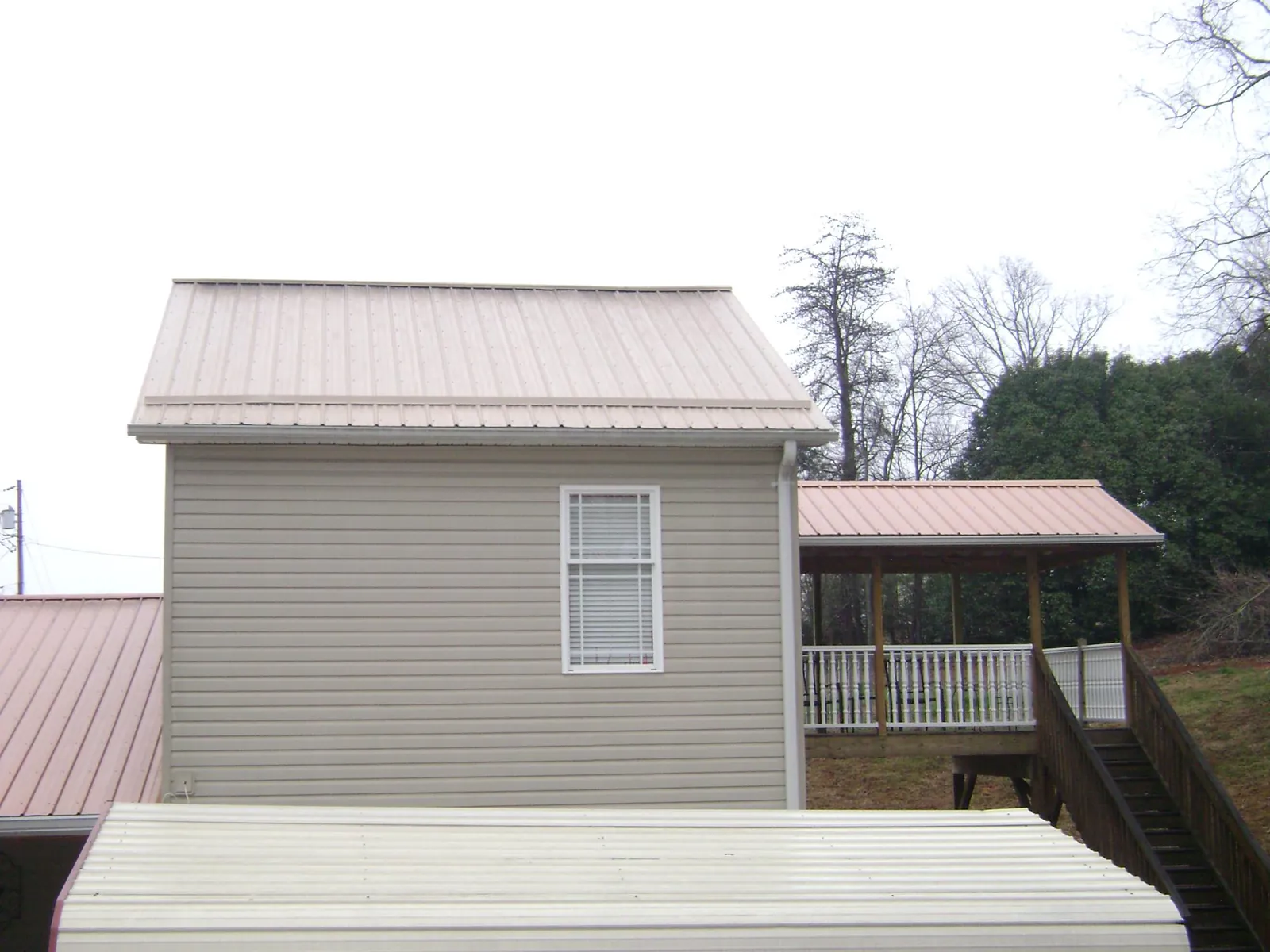 Tan metal roofs on a two story addition and attached porch, from a Roof Replacement job in Grass Lake